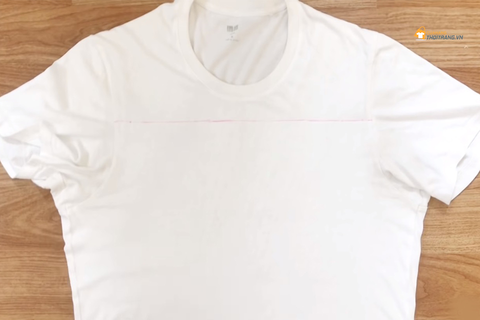 Trải phẳng áo lên mặt bàn, vẽ một đường thẳng nối điểm chính giữa của tay áo.