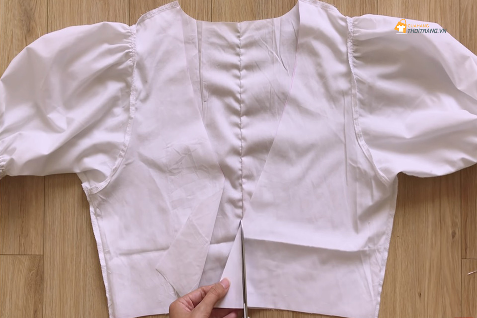 Đặt ngay ngắn chiếc áo sao cho 2 mảnh trước của áo chồng lên nhau. Tại phần xếp chồng lên nhau đó, bạn dùng kéo cắt đi phần vải thừa